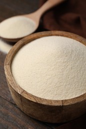 Photo of Uncooked organic semolina in bowl and spoon on wooden table, closeup