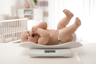 Photo of Cute little baby lying on scales in light room