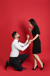 Photo of Man with engagement ring making marriage proposal to girlfriend on red background