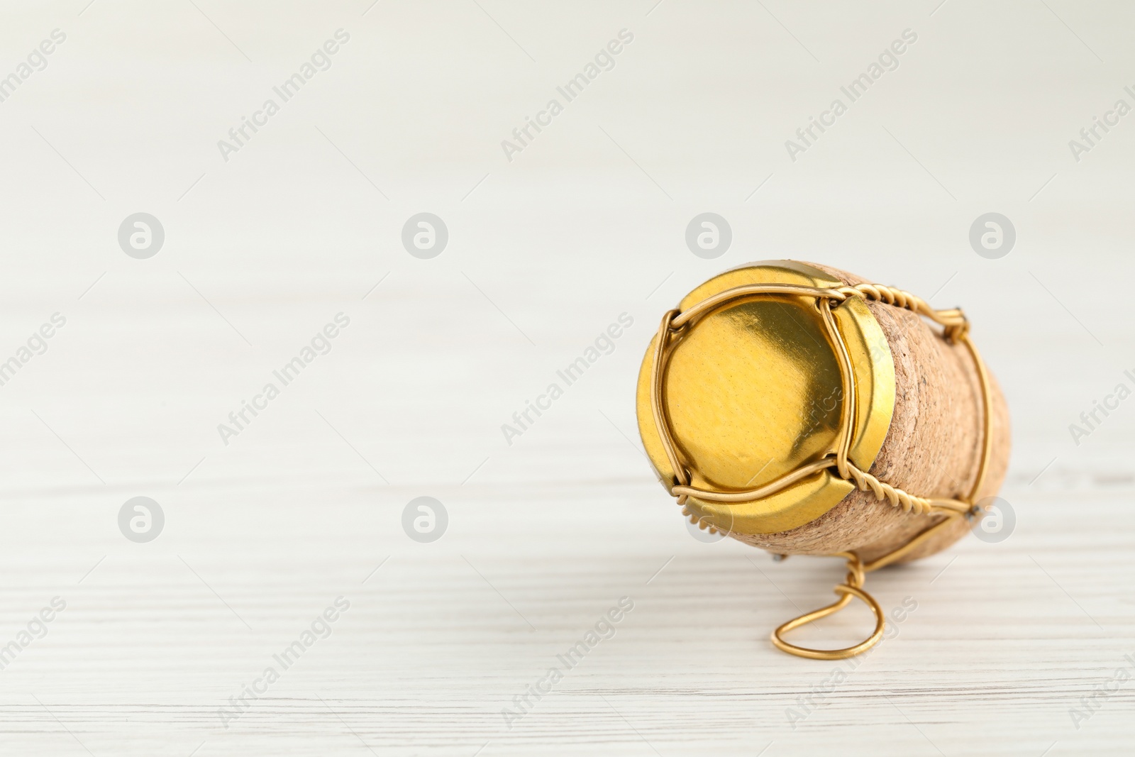 Photo of Cork of sparkling wine and muselet cap on white wooden table, closeup. Space for text