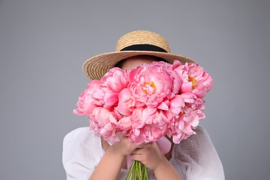 Photo of Young woman covering her face with bouquet of peonies on grey background