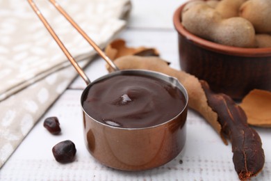 Photo of Measuring cup with tasty tamarind sauce and fresh pods on white wooden table, closeup