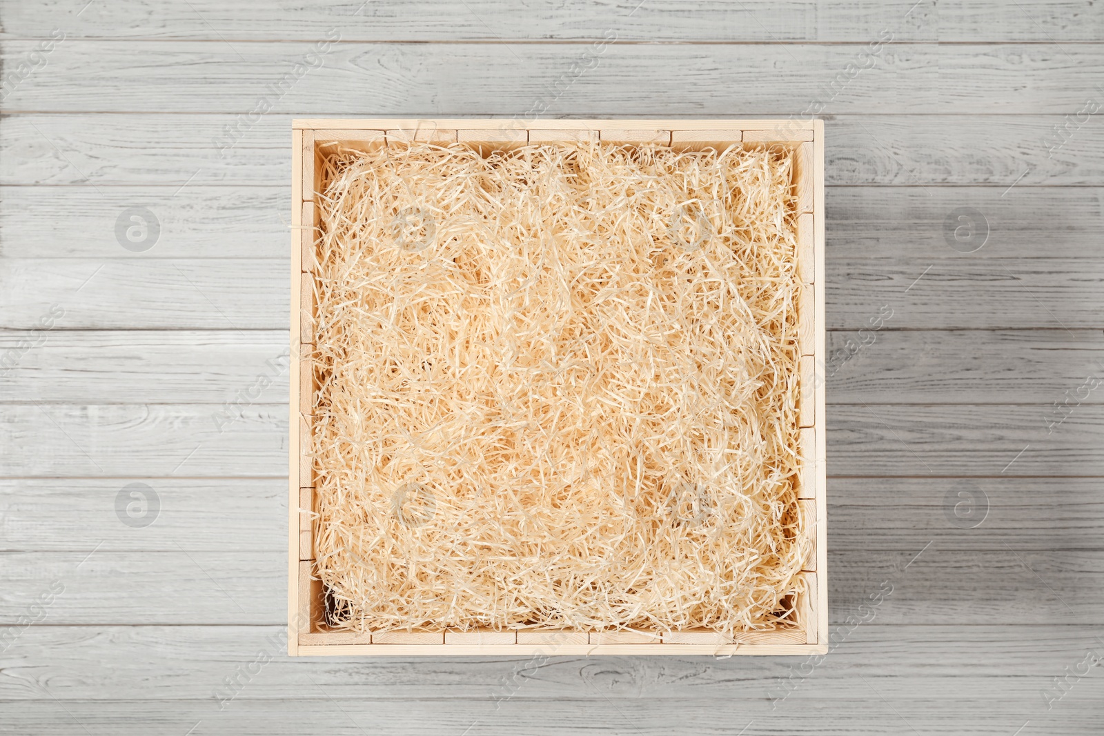 Photo of Wooden crate with filler on light background, top view