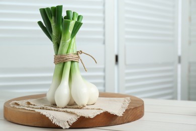 Photo of Bunch of green spring onions on white wooden table. Space for text