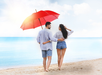 Image of Happy young couple with umbrella for sun protection walking on beach near sea