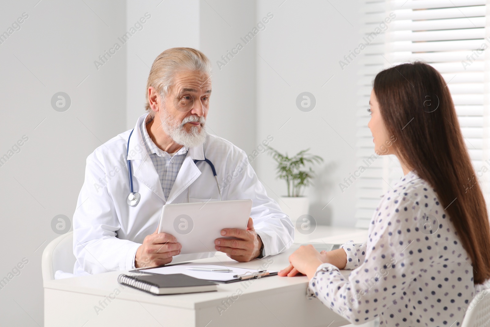 Photo of Senior doctor consulting patient at white table in clinic