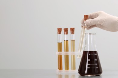 Photo of Scientist taking test tube with brown liquid from stand on light background, closeup. Space for text