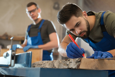 Photo of Professional carpenter making mark on wooden board in workshop