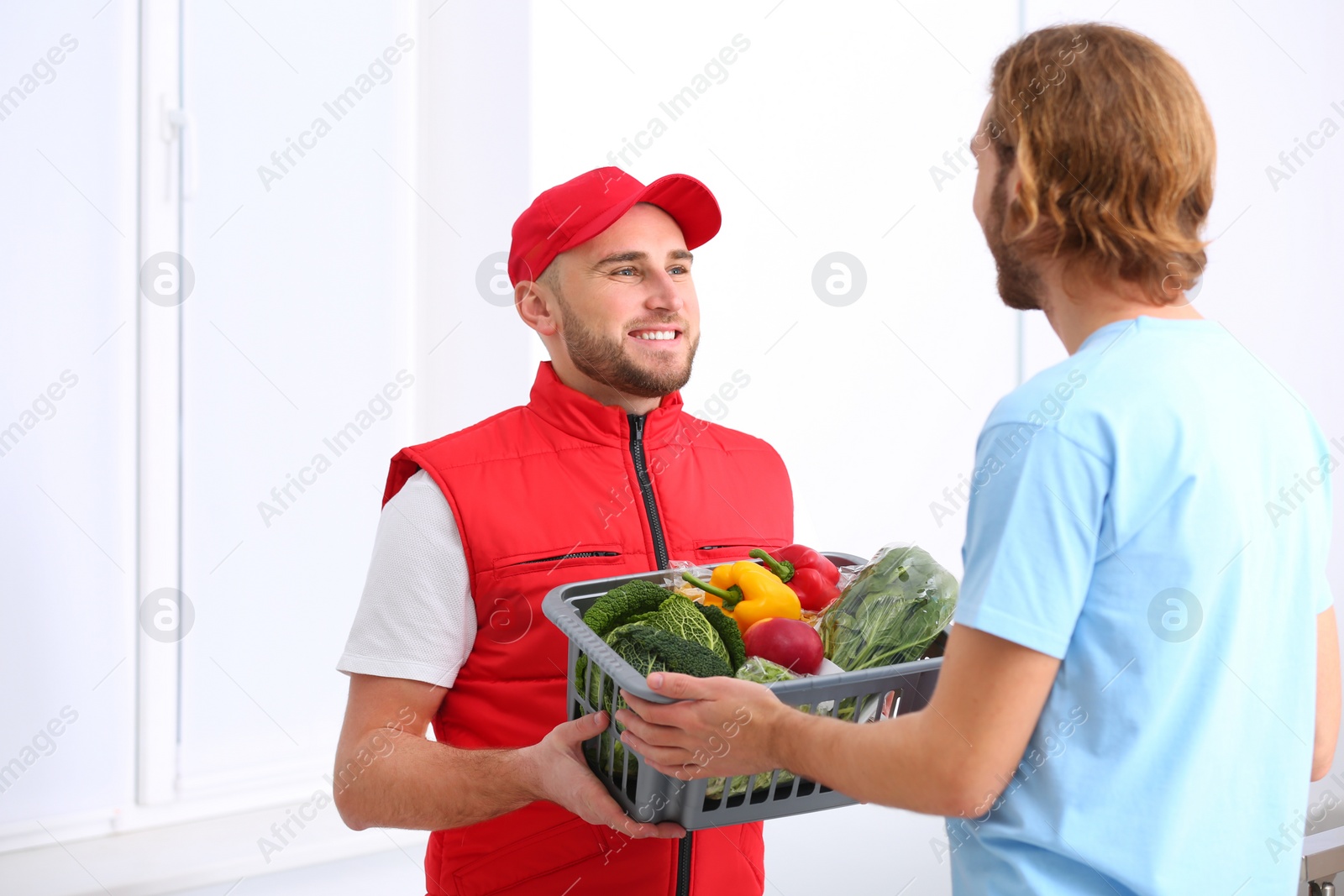 Photo of Courier giving plastic crate with products to customer at home. Food delivery service