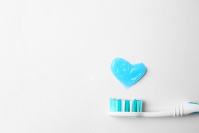 Photo of Heart made with toothpaste and brush on white background, top view. Space for text