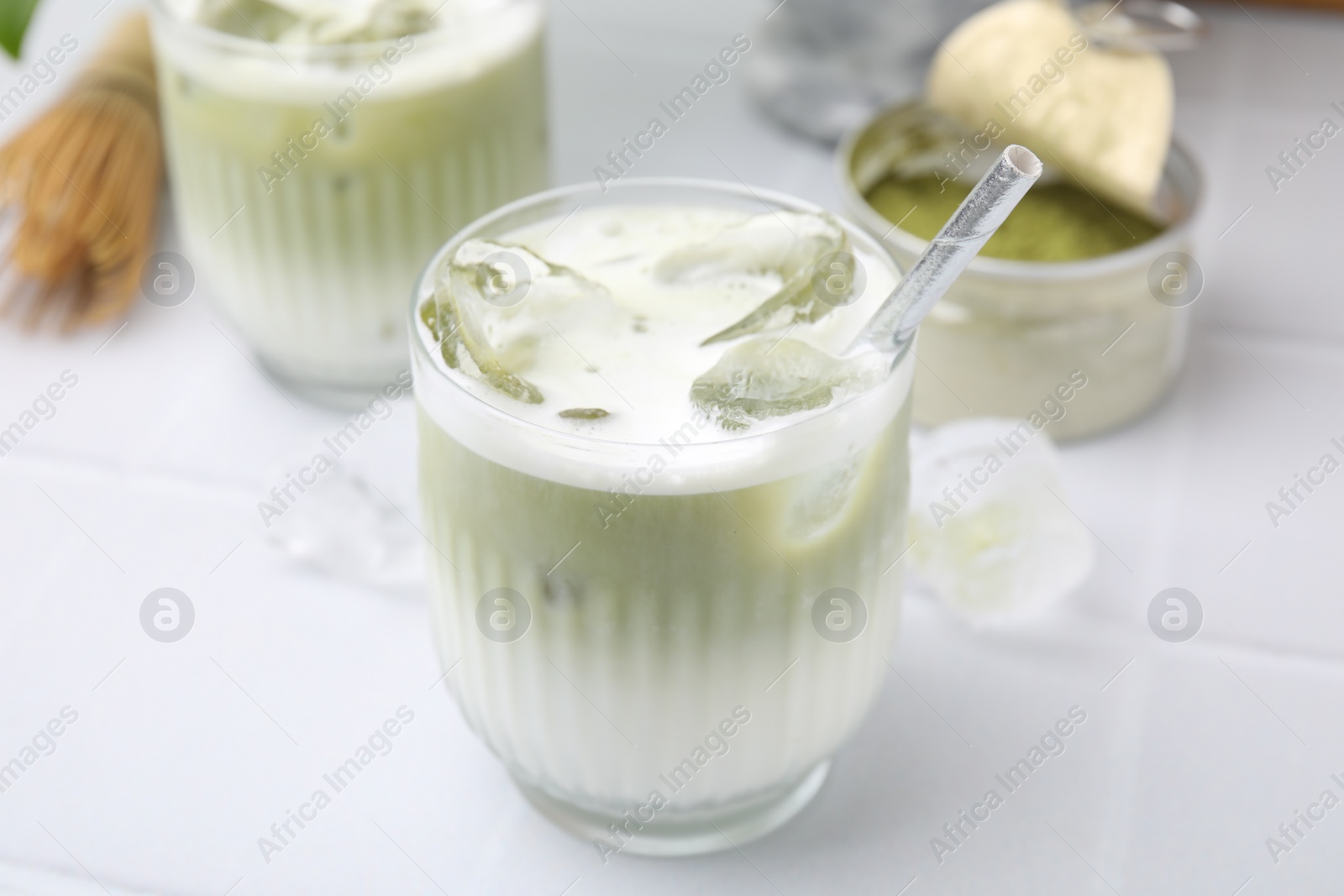 Photo of Glasses of tasty iced matcha latte on white tiled table, closeup