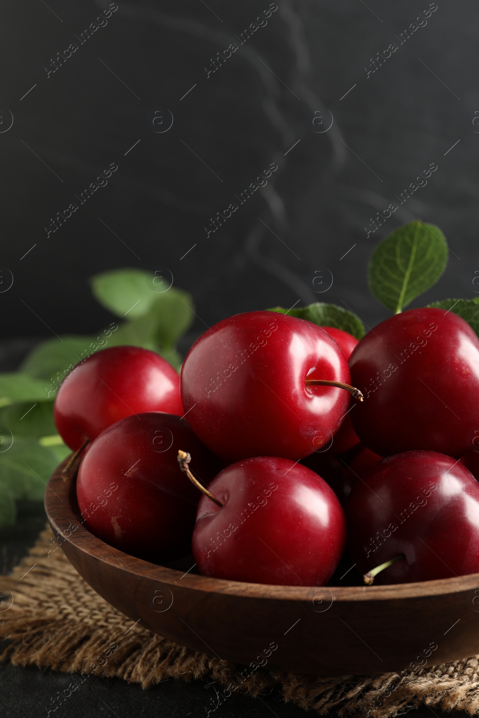 Photo of Delicious ripe cherry plums with leaves on black table