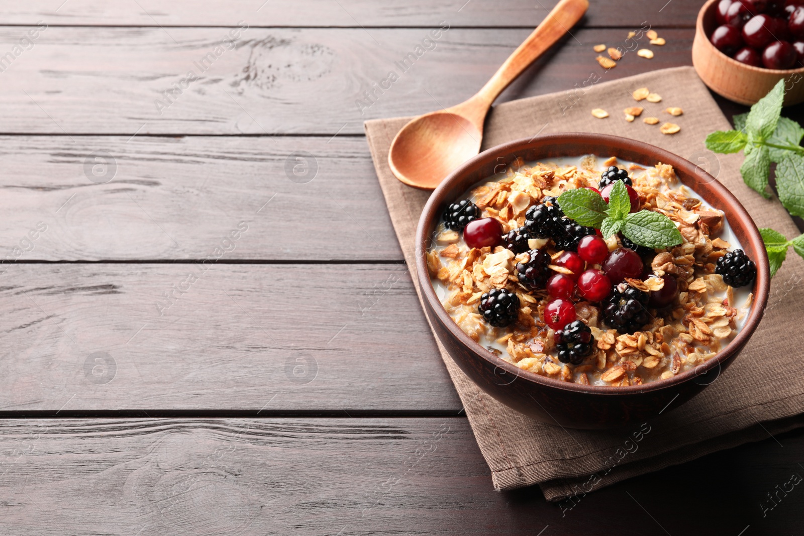 Photo of Bowl of muesli served with berries and milk on wooden table, space for text