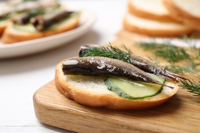 Delicious sandwich with sprats, cucumbers and dill on wooden board, closeup