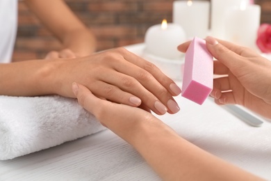 Photo of Manicurist polishing client's nails with buffer at table, closeup. Spa treatment