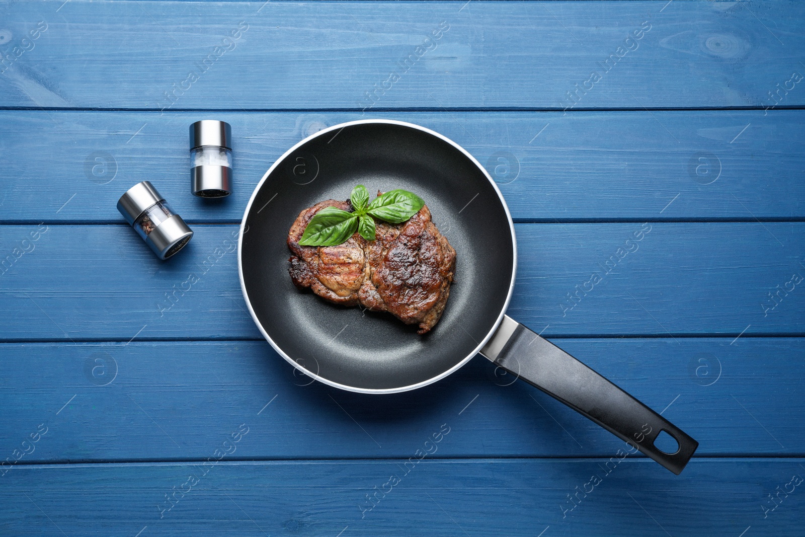 Photo of Frying pan with tasty steak on blue wooden table, flat lay