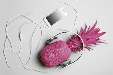 Pineapple with headphones and smartphone on grey background, top view