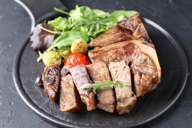 Photo of Delicious grilled beef meat, vegetables and greens on black table, closeup