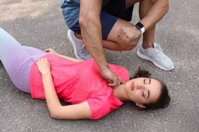 Young man checking pulse of unconscious woman on street