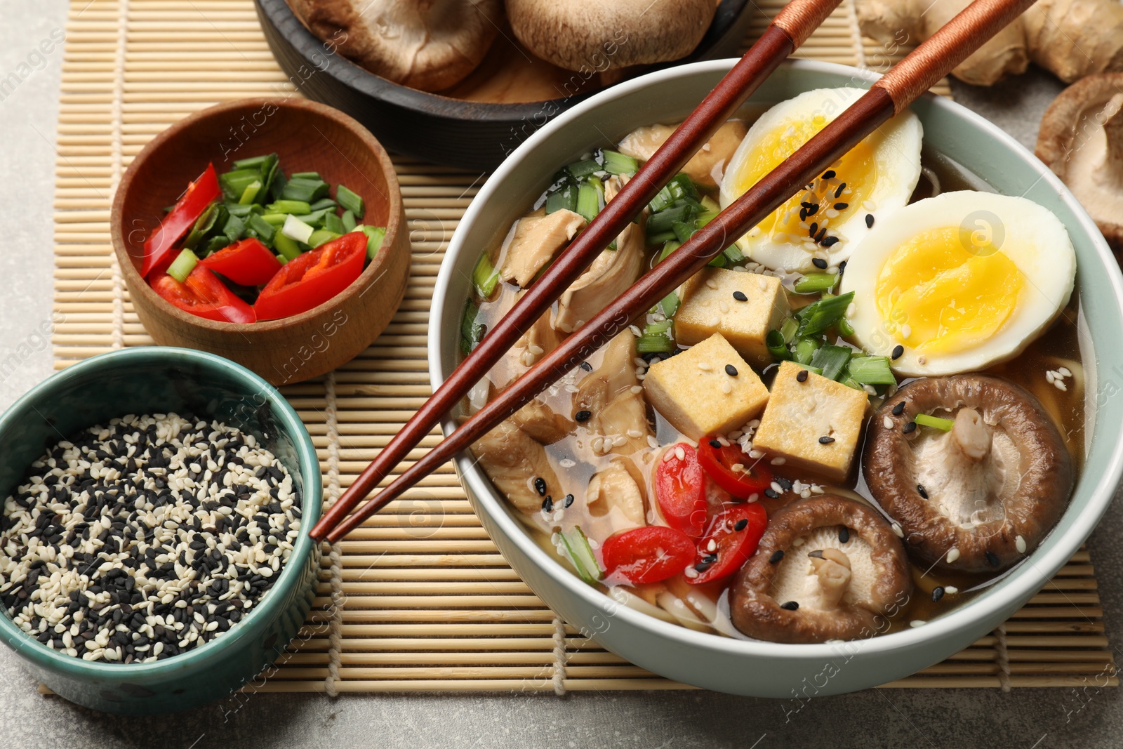 Photo of Bowl of delicious ramen and ingredients on grey table. Noodle soup