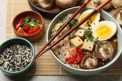 Bowl of delicious ramen and ingredients on grey table. Noodle soup