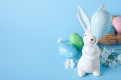 Photo of Easter bunny figure, flowers and dyed eggs on light blue background. Space for text