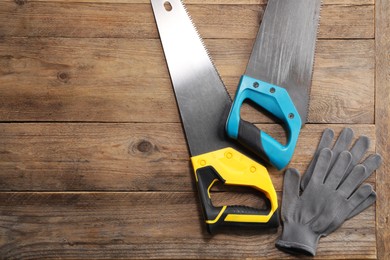 Saws with colorful handles and gloves on wooden background, flat lay. Space for text