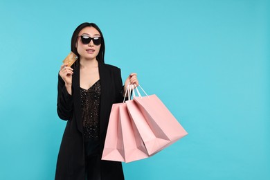 Photo of Smiling woman with shopping bags and credit card on light blue background. Space for text
