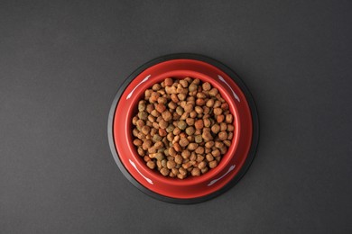 Photo of Dry dog food in feeding bowl on black background, top view