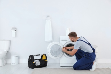 Young plumber fixing washing machine in bathroom