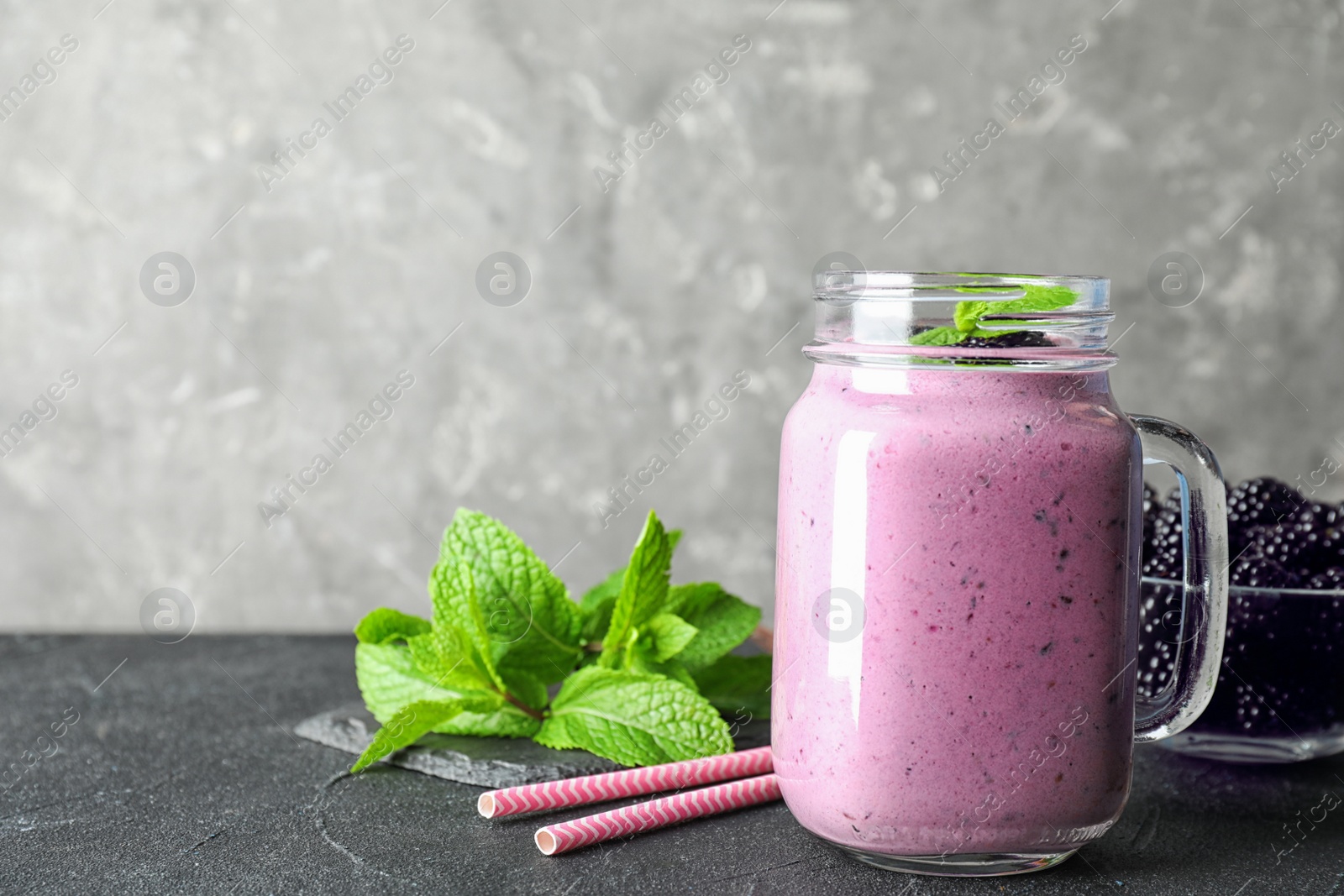 Photo of Delicious blackberry smoothie in mason jar on black table against grey background. Space for text