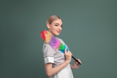 Photo of Young chambermaid with dusting brush on color background