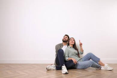 Young couple sitting on floor near white wall indoors. Space for text