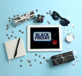 Photo of Flat lay composition with tablet, gifts and accessories on light blue background. Black Friday sale