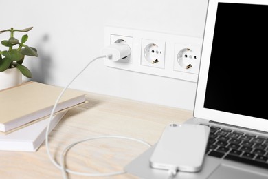 Photo of Laptop and smartphone charging on wooden table