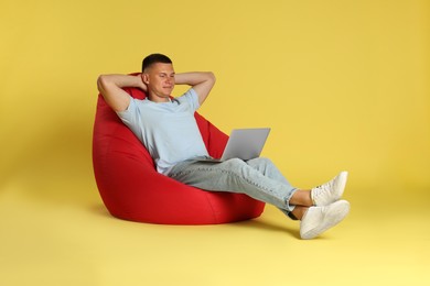 Photo of Handsome man with laptop on red bean bag chair against yellow background