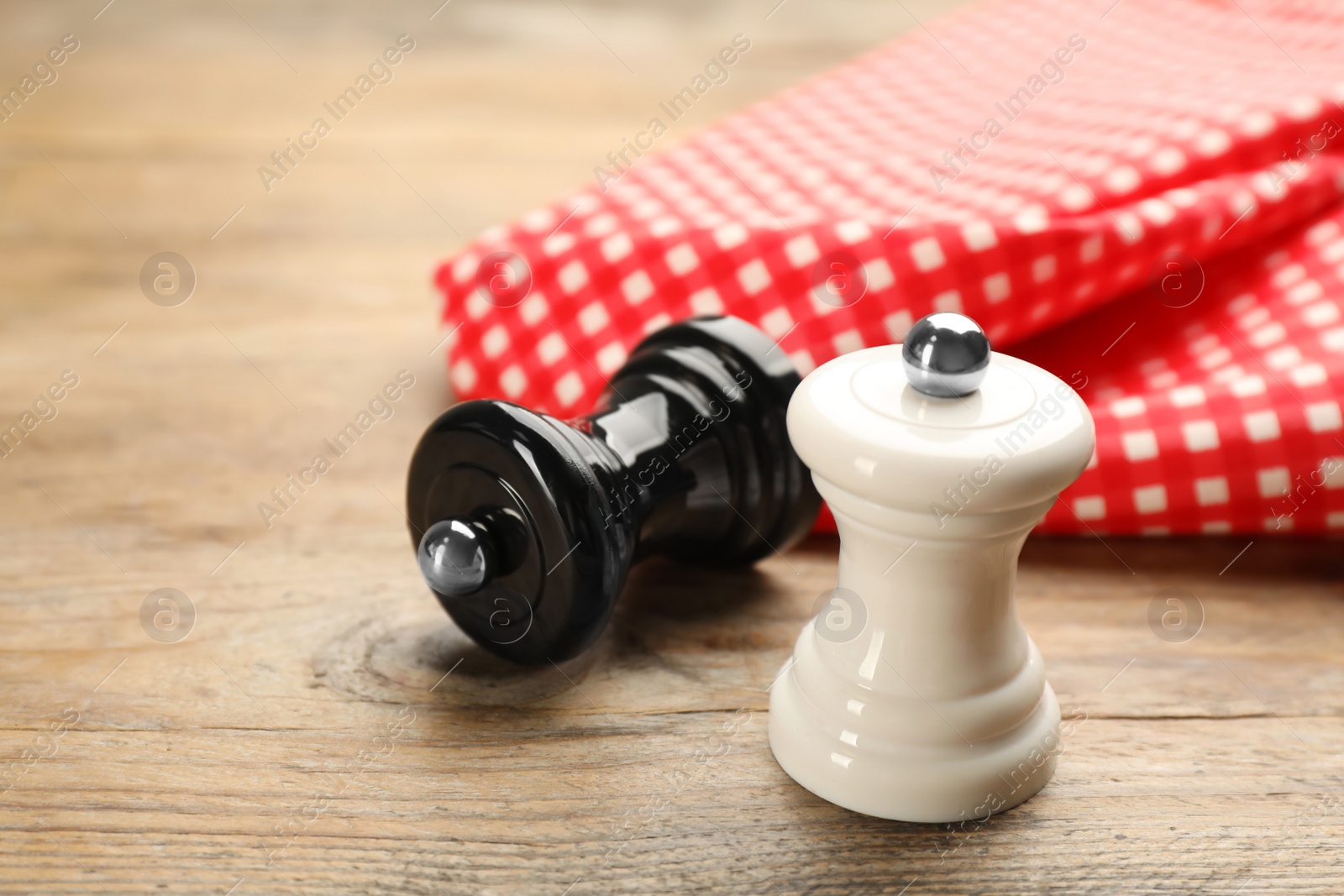 Photo of Salt and pepper shakers with napkin on wooden table, closeup. Spice mill