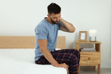 Man suffering from neck pain after sleeping on uncomfortable mattress at home