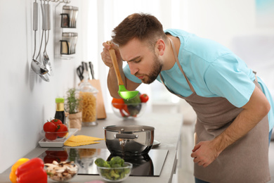 Young man cooking delicious soup in kitchen