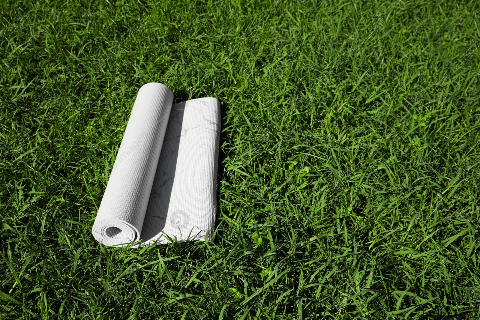 Photo of Karemat or fitness mat on green grass outdoors, space for text