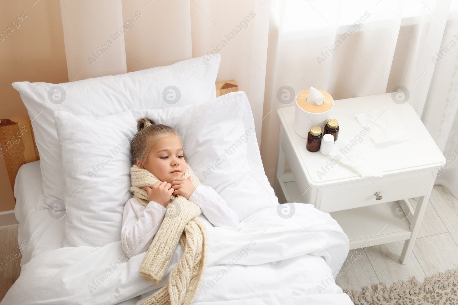 Photo of Sick girl with scarf lying in bed indoors, above view. Cold symptoms