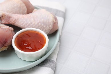 Photo of Fresh marinade and raw chicken drumsticks on white tiled table, closeup. Space for text