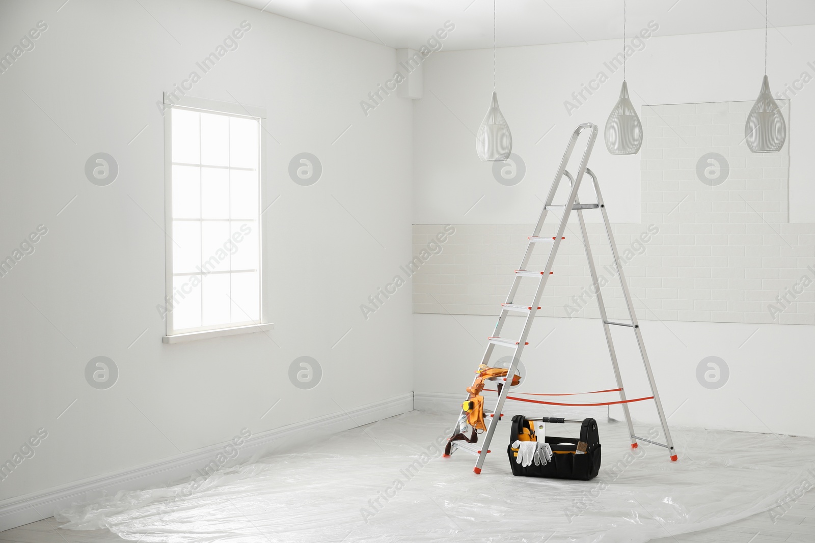 Photo of Stepladder and different tools near wall in room. Interior renovation