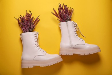 Photo of Pair of stylish leather shoes with heather flowers on yellow background, flat lay