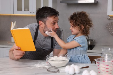 Cute little girl and her father with recipe book having fun in kitchen