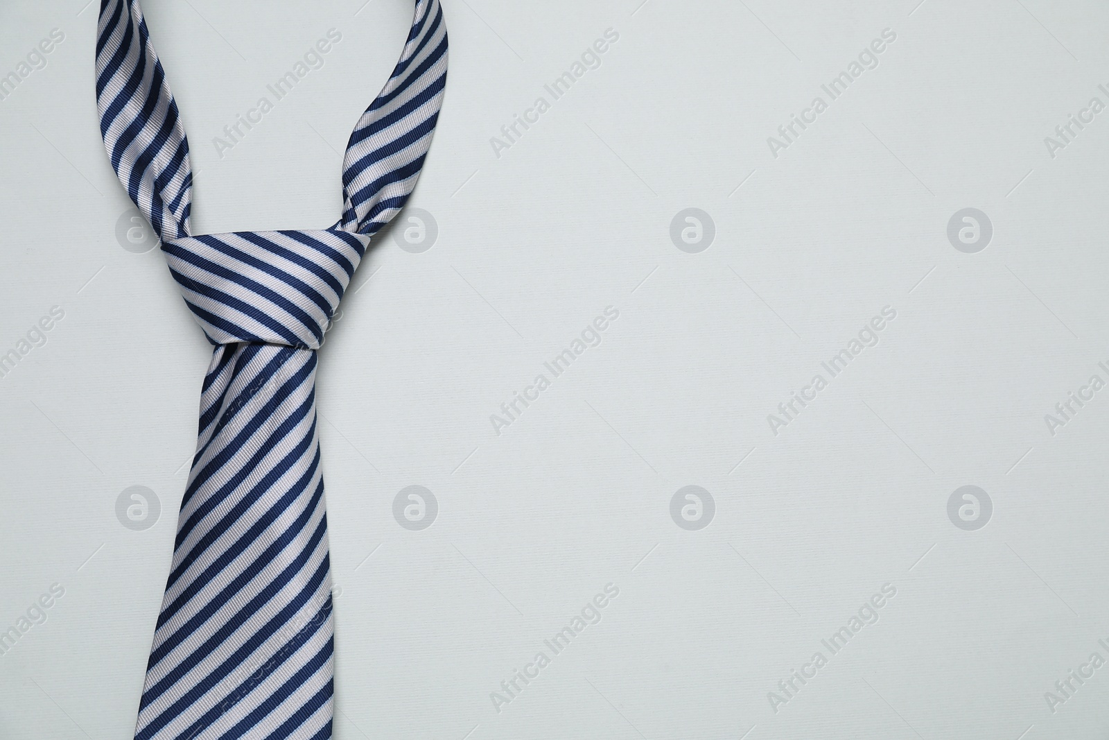 Photo of Striped necktie on light background, top view. Space for text