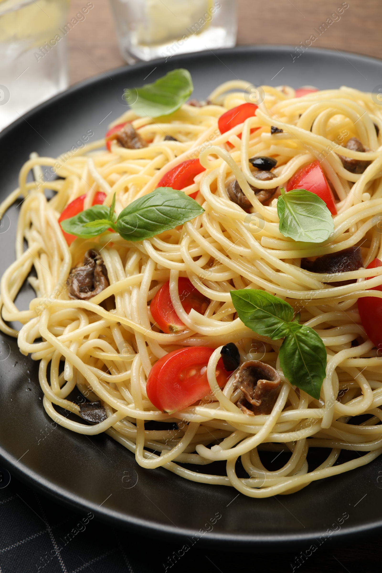 Photo of Delicious pasta with anchovies, tomatoes and basil on plate