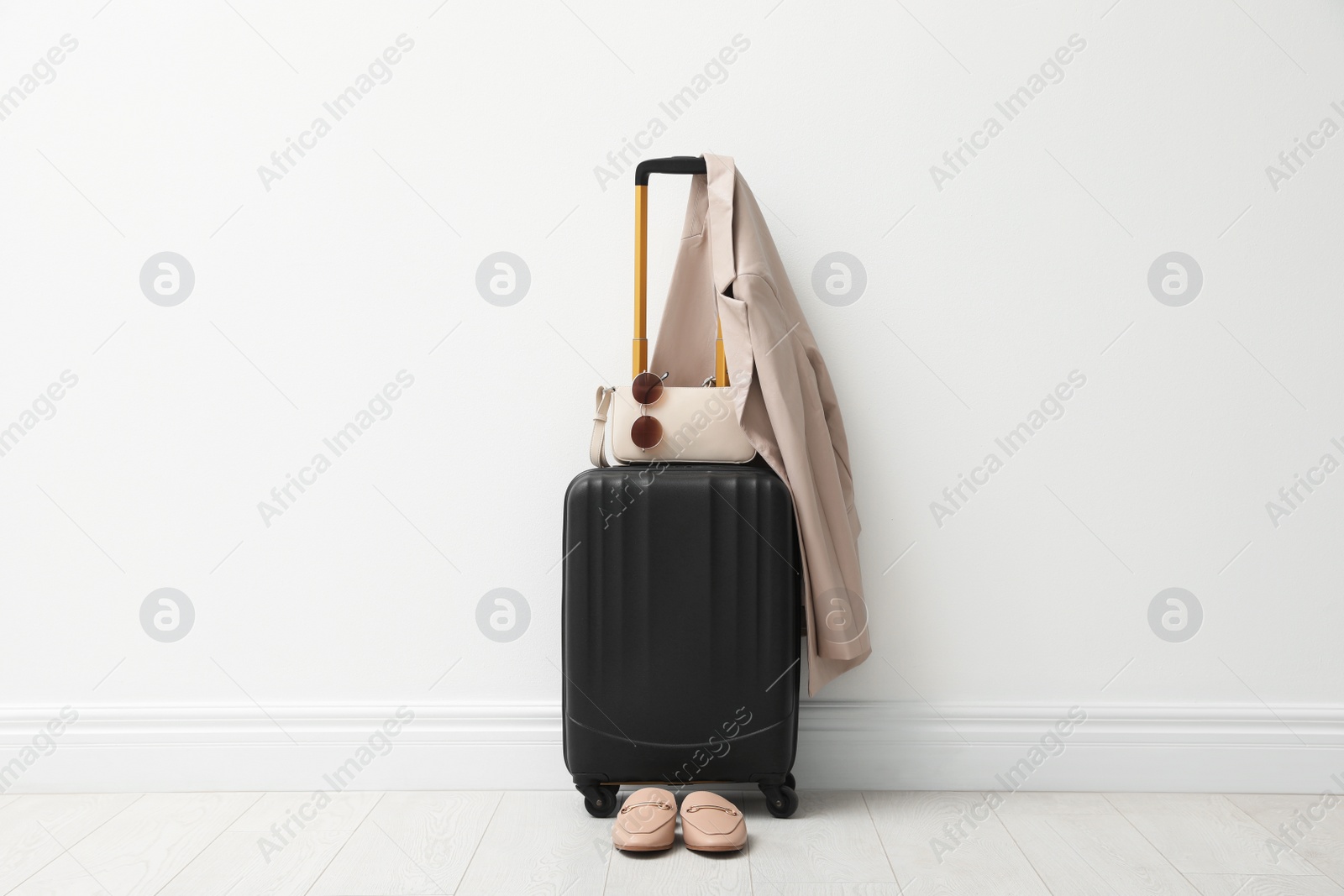 Photo of Suitcase packed for trip, shoes, jacket and accessories near white wall indoors