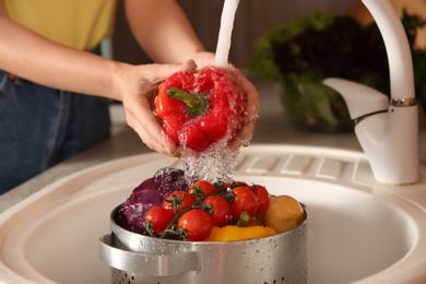 Photo of Woman washing fresh red bell pepper in kitchen sink, closeup