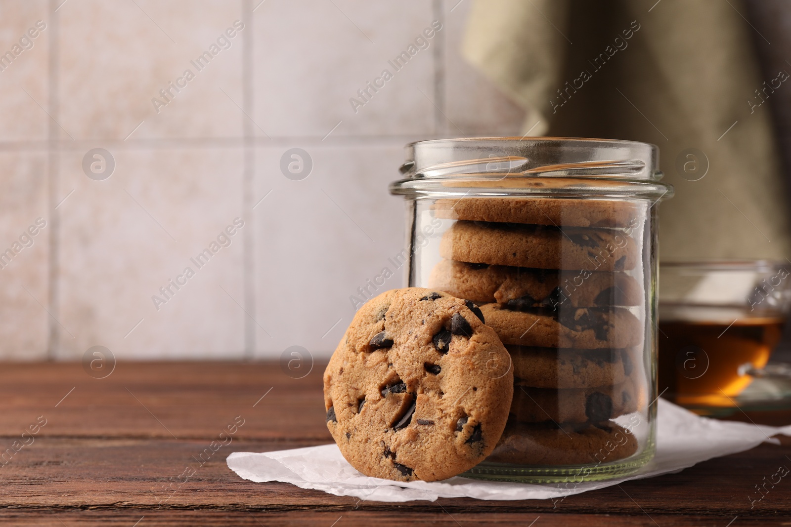 Photo of Glass jar with delicious chocolate chip cookies and tea on wooden table. Space for text